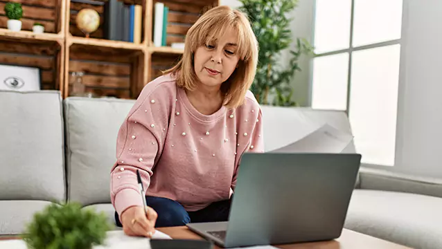 Sitting on her couch in front of a laptop on the coffee table, a woman jots down a note on a piece of paper. Experienced lawyers can help you apply for disability in Georgia.