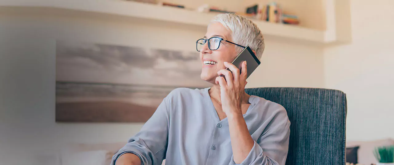 A woman sits in her home, talks on the phone and smiles. This page gives contact information for Georgia disability law firm Silver & Archibald.