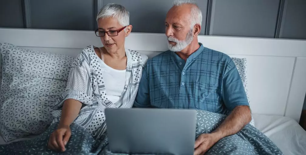 A woman and man sit in bed. The man has a laptop on his legs. If you’re trying to understand the qualifications for Social Security Disability, a lawyer can help.