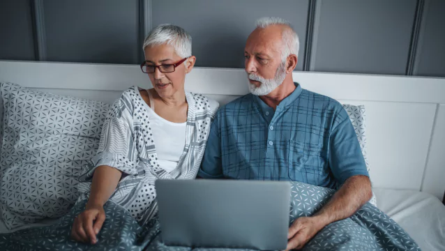 A woman and man sit in bed. The man has a laptop on his legs. If you’re trying to understand the qualifications for Social Security Disability, a lawyer can help.