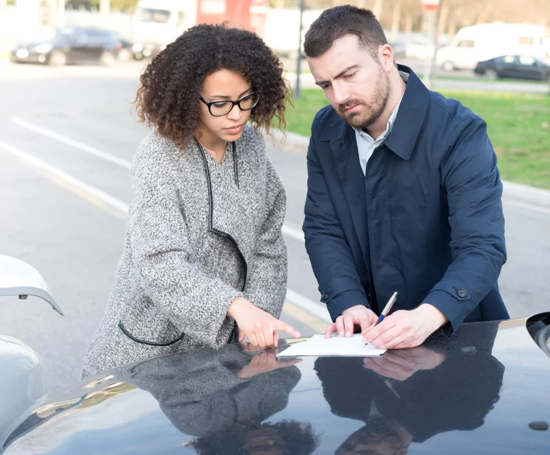 A woman and man look at papers on the hood of a car. She points while he writes. Personal injury claims can come out of many different situations.