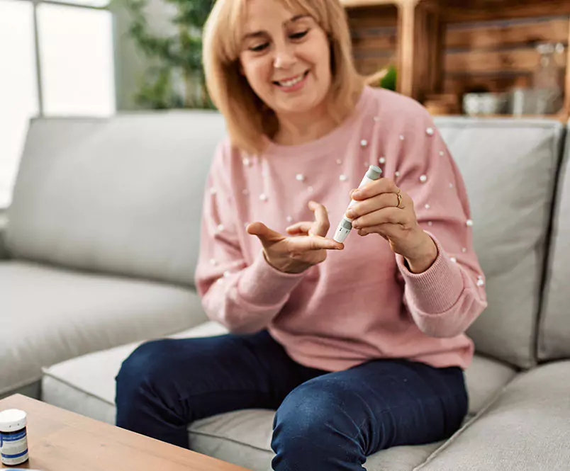 As she sits on her couch, a woman touches a blood sugar meter to her finger. Disability lawyers help with the benefits application process.