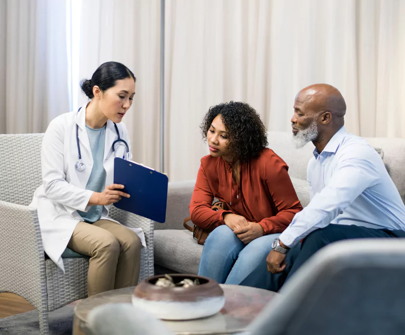 Sitting on a couch in a waiting room, a couple listens to a doctor as she shows them information on a clipboard. PI attorneys gather the medical evidence you need for an injury claim.