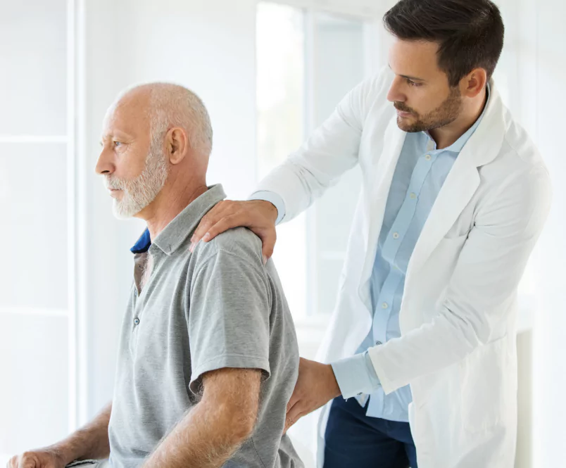 As a man sits on an exam table, a doctor presses on his back. Multiple kinds of impairments can qualify for disability benefits.